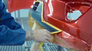 Painter removing tape from freshly painted red bumper - auto paint repair - Harley Collision Centers