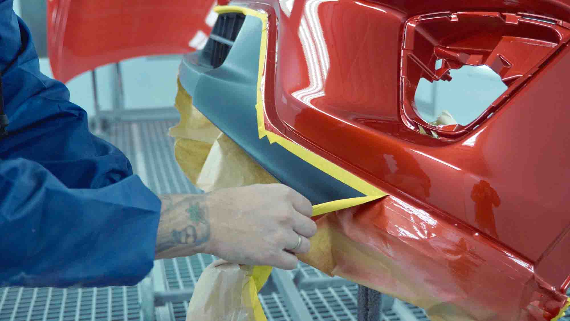 Painter removing tape from freshly painted red bumper – auto paint repair – Harley Collision Centers Painter removing tape from freshly painted red bumper - auto paint repair - Harley Collision Centers